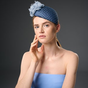 May include: A woman wearing a blue and white hat with a flower detail. She is wearing a light blue strapless top and has her hand on her cheek.