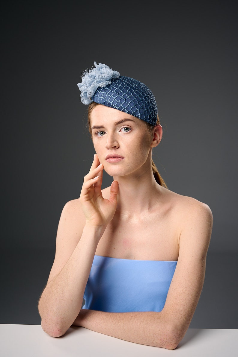 May include: A woman wearing a blue and white hat with a flower detail. She is wearing a light blue strapless top and has her hand on her cheek.