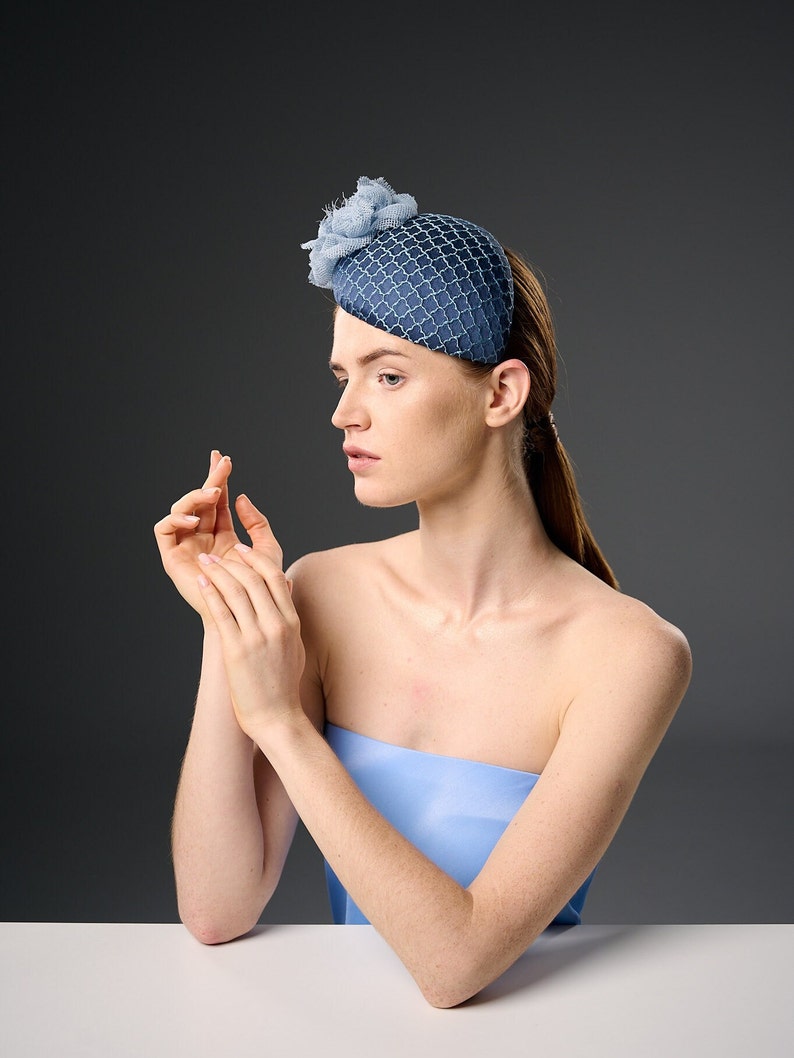May include: A woman wearing a blue and white patterned hat with a flower accent. She is wearing a strapless blue top and has her hair pulled back.