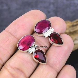 May include: Two pairs of gemstone earrings. Each earring features a large oval ruby and a smaller, teardrop-shaped garnet. The gemstones are set in silver. The text "mohanjewels" is visible.