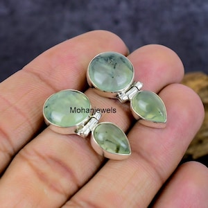 May include: A pair of silver earrings with green gemstone drops. The earrings feature a round green stone at the top and a teardrop-shaped green stone hanging below.