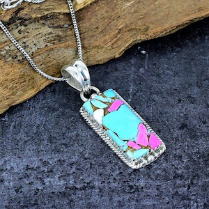 May include: A rectangular pendant necklace with a silver chain. The pendant features a turquoise, pink, white, and gold stone set in a silver frame. The stone has a unique, colorful pattern.