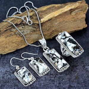 May include: A silver necklace, pendant, ring, and earrings set. The jewellery features rectangular stones with a black and white pattern, set in silver. The earrings have a hook closure. The ring and pendant are connected to a silver chain.