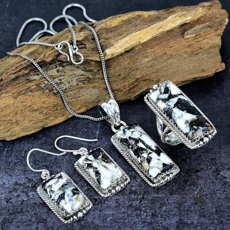Puede incluir: Un conjunto de collar, colgante, anillo y pendientes de plata. Las joyas presentan piedras rectangulares con un patr&oacute;n en blanco y negro, engastadas en plata. Los pendientes tienen cierre de gancho. El anillo y el colgante est&aacute;n conectados a una cadena de plata.