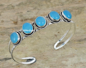 May include: Silver bangle bracelet featuring five light blue oval-shaped gemstones. The bracelet has a delicate, intricate design.