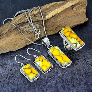 May include: A jewelry set featuring a necklace, earrings, and a ring. Each piece has a rectangular, yellow and green stone set in a silver-colored metal frame. The necklace has a delicate chain.