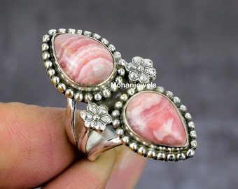 May include: A silver ring with two pink and white striped gemstones set in a flower design. The ring is on a finger.