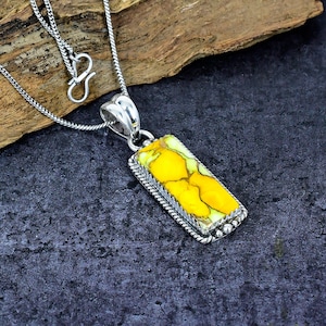 May include: Silver pendant necklace featuring a rectangular yellow stone with a unique pattern. The stone is set in a silver frame with a rope-like border and small bead accents. The necklace has a delicate silver chain.
