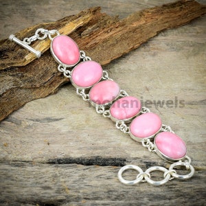 May include: A silver bracelet with pink oval-shaped gemstones. The bracelet has a toggle clasp.