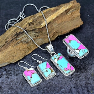 May include: A jewelry set featuring a necklace, earrings, and ring. Each piece has a rectangular turquoise, pink, and white stone set in a silver-colored metal. The necklace has a chain, and the earrings are hook-style.