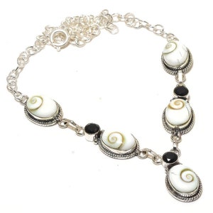 Peut inclure: Un collier en argent avec un pendentif en coquille blanche et des accents de pierres précieuses noires. Le collier est doté d'une chaîne avec un fermoir à homard.