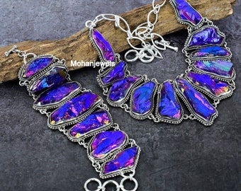 Puede incluir: Un conjunto de collar y pulsera de plata con acentos de piedras preciosas iridiscentes de color púrpura y azul. El collar y la pulsera están hechos de plata y presentan un diseño de eslabones de cadena.