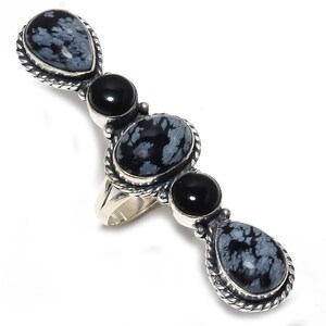 Puede incluir: Un anillo de plata con tres piedras de obsidiana copo de nieve negras y grises y dos piedras de ónix negras. El anillo está engastado en una banda de plata con un diseño de cuerda.
