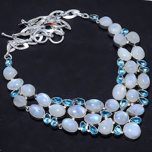 May include: A silver necklace with a layered design featuring white moonstone and blue topaz gemstones. The necklace has a lobster claw clasp.