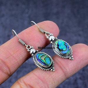 May include: A pair of silver dangle earrings featuring iridescent abalone shell oval-shaped stones. The earrings have a twisted wire design and a beaded accent.