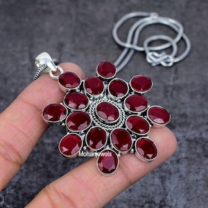 May include: A silver pendant necklace featuring a large, red gemstone cluster in the shape of a flower. The pendant is surrounded by smaller, red gemstones. The necklace is on a silver chain.