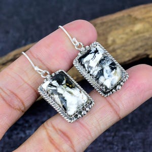 Puede incluir: Un par de pendientes rectangulares con una piedra blanca, negra y gris engastada en un marco plateado. Los pendientes tienen un borde decorativo en forma de cuerda y un cierre de gancho. El patr&oacute;n de la piedra es &uacute;nico.