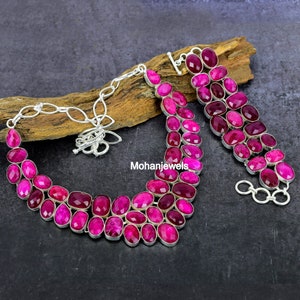May include: A necklace and bracelet set featuring faceted, deep pink gemstone beads set in silver-toned metal. The necklace has a multi-strand design with a toggle clasp, and the bracelet consists of two rows of matching pink stones with a toggle closure.