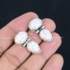 May include: A pair of silver earrings with white shell-like stones. The stones are oval and teardrop shaped and have a textured surface.