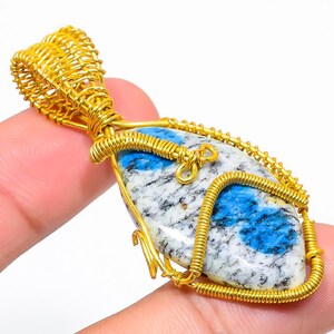 Può includere: Un ciondolo avvolto in filo d'oro con una pietra preziosa di cianite blu e bianca. Il ciondolo è di forma ovale e presenta un delicato design in filo.
