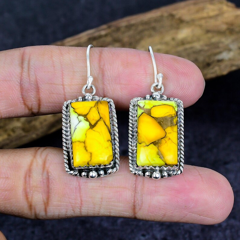 May include: A pair of silver-toned earrings with rectangular yellow and green stone insets. The stones have a cracked appearance and are framed by a twisted rope design. The earrings are suspended from a simple hook.
