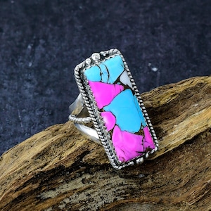 May include: A rectangular silver ring with a colorful stone inlay. The stone features a mosaic of pink, light blue, and white sections. The ring has a twisted rope design around the stone and a decorative band.