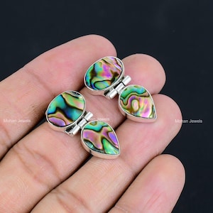 Könnte beinhalten: Ein Paar silberne Ohrringe mit schillernden Abalone-Muschel-Akzenten. Die Ohrringe sind tropfenförmig und haben ein Scharnierdesign.