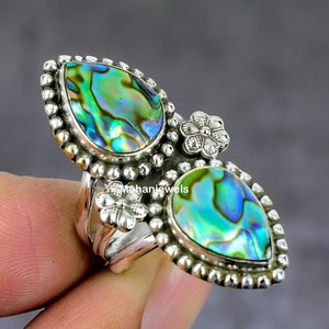 May include: A silver ring with two pear-shaped abalone shell stones and a silver flower design. The ring is set with a beaded border.
