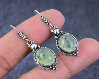 May include: A pair of silver earrings with green gemstone drops. The earrings have a delicate, ornate design with a twisted wire detail.