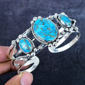 May include: A silver cuff bracelet featuring three oval turquoise stones with gold flecks. The stones are set in ornate silver settings with decorative accents. The bracelet has a wide, open design.
