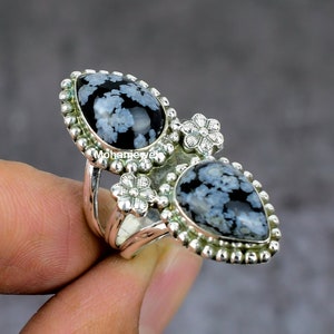 May include: A silver ring with two snowflake obsidian stones and floral accents.