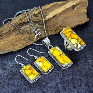 May include: A jewelry set featuring a necklace, earrings, and ring. Each piece has a rectangular, yellow and green stone set in a silver-colored metal frame. The necklace has a delicate chain.