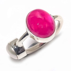 Pode incluir: Um anel de prata com uma grande pedra preciosa ovalada de cor rosa brilhante. O anel tem uma pérola no lado.