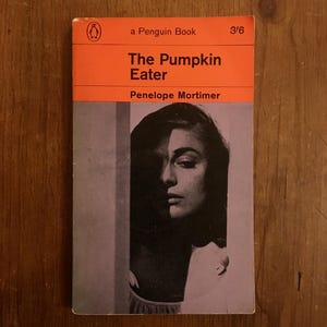 May include: Vintage Penguin Book cover for "The Pumpkin Eater" by Penelope Mortimer. The cover features a black and white portrait of a woman's face, with the title in white text on a bright orange background. The Penguin logo is visible.