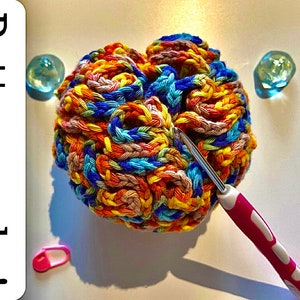 May include: A colourful crocheted ball with a pink crochet hook. The ball is made with multiple colours of yarn, including orange, yellow, blue, and brown. The text "Pattern only!" is visible in the image.