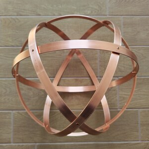 May include: A copper-coloured, spherical sculpture made of intersecting curved metal bands. The bands are joined at various points, creating a three-dimensional geometric design. The sculpture is mounted on a light brown tiled wall.