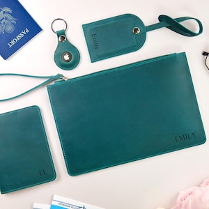 May include: A teal leather travel set including a passport holder, luggage tag, AirTag holder, and a zippered pouch. The pouch and luggage tag are personalized with the name "Emily". A blue passport and glasses are also in the image.