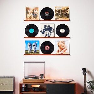 May include: A display of vinyl records on wooden shelves, showcasing album covers and black records. A turntable and stereo equipment are visible below. The records include album covers with various designs and colors, creating a vintage music theme.