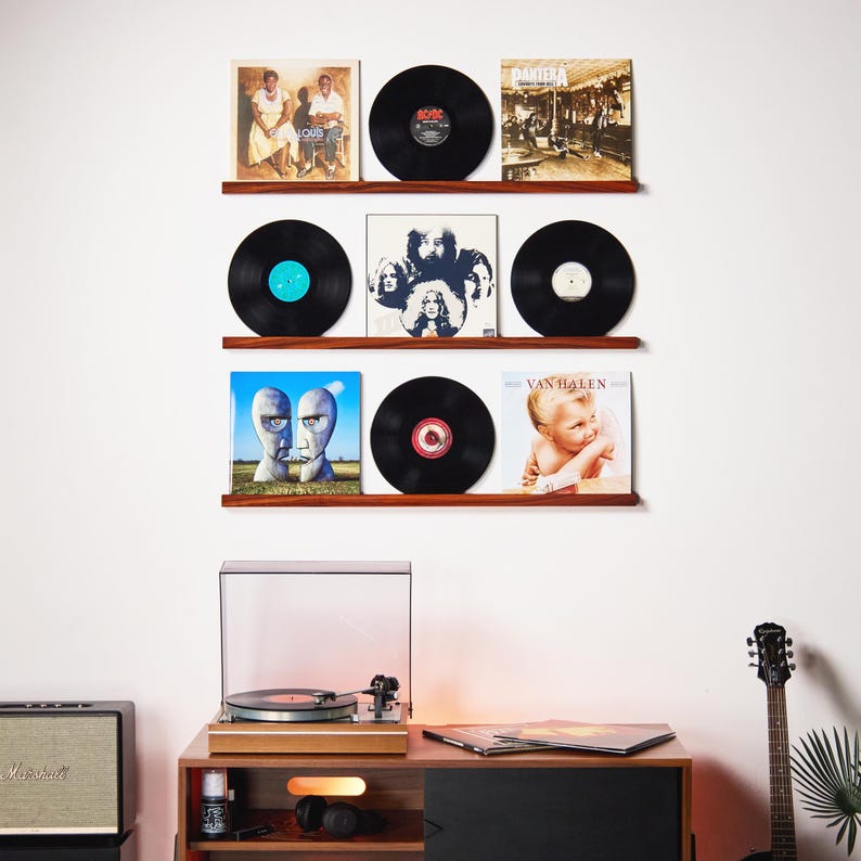 May include: A display of vinyl records on wooden shelves, showcasing album covers and black records. A turntable and stereo equipment are visible below. The records include album covers with various designs and colors, creating a vintage music theme.
