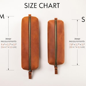 May include: Two brown leather pencil cases with brass zippers are displayed against a white background. The larger case, labeled "M", measures 9.4" x 2.7" x 2.1". The smaller case, labeled "S", measures 7.8" x 2.7" x 2.1". The text "SIZE CHART" is at the top.
