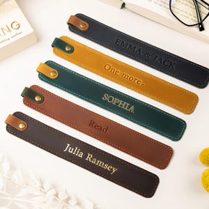 May include: Leather bookmarks in various colors, including black, mustard yellow, and brown. Each bookmark has a stitched border and a snap closure. Some bookmarks are personalized with names or phrases like "Emma & Jack" and "Read."