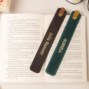 May include: Two leather bookmarks, one brown and one green, rest on an open book. The brown bookmark has "Julia Ramsey" in gold lettering, and the green one reads "Sophia". Each has a leather loop.