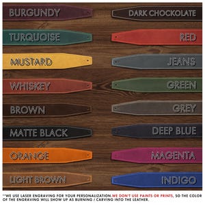 K&ouml;nnte beinhalten: Eine Auswahl an Gitarrengurten aus Leder in verschiedenen Farben, darunter Burgunder, T&uuml;rkis, Senf, Whiskey, Braun, Mattschwarz, Orange, Hellbraun, Dunkle Schokolade, Rot, Jeans, Gr&uuml;n, Grau, Tiefblau, Magenta und Indigo. Jeder Gurt ist mit seinem Farbnamen beschriftet.