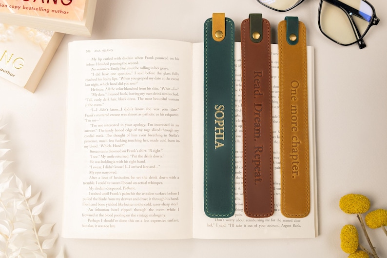 May include: Three leather bookmarks in green, brown, and gold, each with a different embossed message. The green bookmark says "SOPHIA", the brown one says "Read. Dream. Repeat.", and the gold one says "One more chapter."
