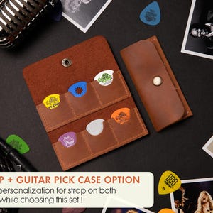 K&ouml;nnte beinhalten: Ein braunes Leder-Gitarrenplektrum-Etui mit mehreren Taschen, das bunte Gitarrenplektren enth&auml;lt. Daneben befindet sich ein passendes Lederetui. Das Bild enth&auml;lt ein Mikrofon, ein Gitarrenkabel und Fotos mit dem Text "STRAP + GUITAR PICK CASE OPTION".
