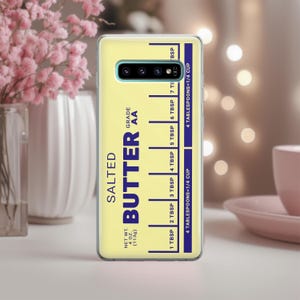 May include: A yellow phone case with a blue and white design that says "Salted Butter Grade AA" and has a measurement chart for tablespoons and cups.
