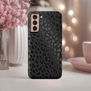 May include: Black phone case with a leopard print design. The case has a raised camera bump with three lenses.