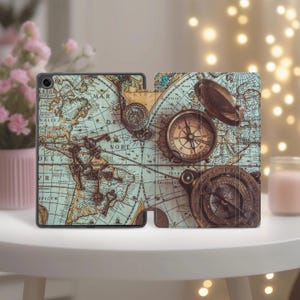 Może przedstawiać: Etui na tablet z motywem mapy w stylu vintage, ozdobione zabytkowymi kompasami i kluczami. Otwarte etui ukazuje mapę świata w odcieniach niebieskiego, brązowego i beżowego. Projekt nawiązuje do podróży i eksploracji.