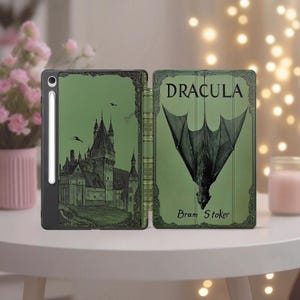 Puede incluir: Funda verde para tableta con una ilustración de castillo y el título "DRACULA" con un gráfico de murciélago. La funda está abierta, revelando el interior y el lomo. También es visible el nombre del autor, Bram Stoker.
