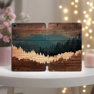 May include: A tablet case with a wooden design featuring a mountain and forest landscape. The case is brown with a teal and dark green forest scene. The case is open, showing the inside and outside design.